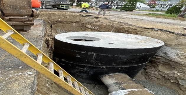 In a dug trench, a large, round container has a pipe running into it.