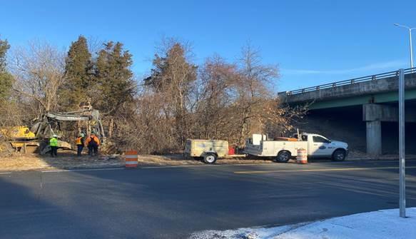 From the other side of the street, a truck is parked near an overpass. Behind the truck, workers survey the area.