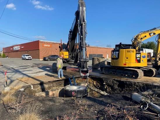 In a parking lot, excavators work to dig an access pit.