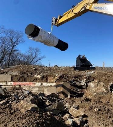 A crane lifts a large black pipe section into the air.