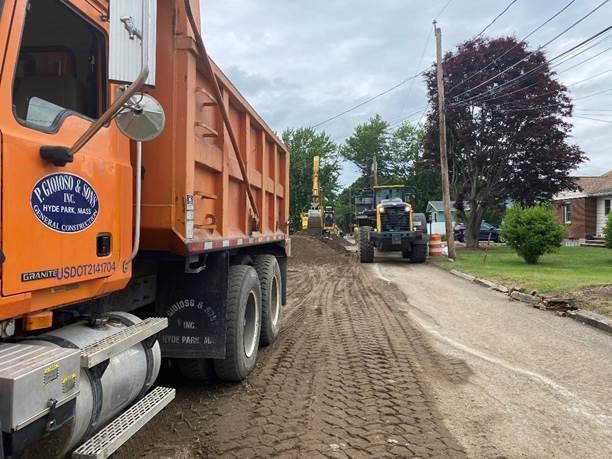 An orange dump truck drives along a dirt residential street.