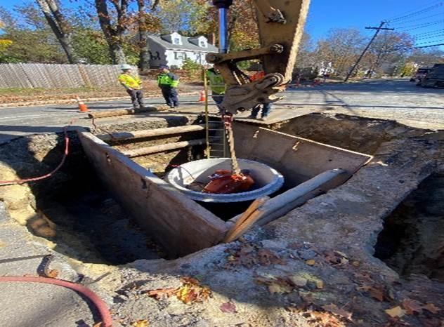In a pit in the street, a crane appears to be chained to an object resting in the centre of a large cylinder.