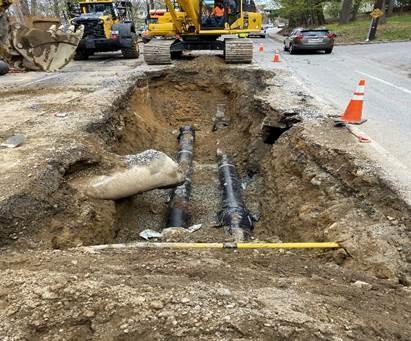 Two parallel pipes run underground, seen in a pit in the road.