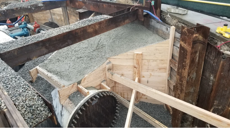 In a trench in the ground, wooden supports hold a pile of dirt over a white pipe.