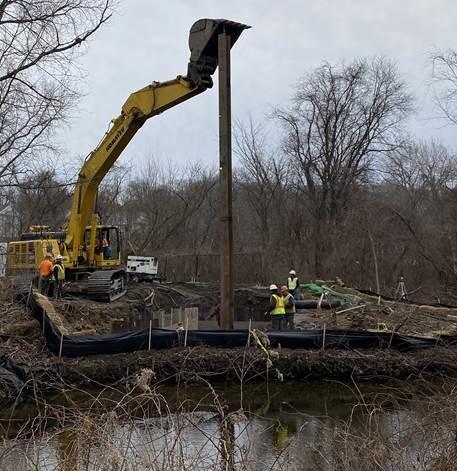 An excavator pushes a long pipe down into the ground.
