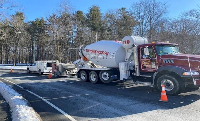 A concrete mixer parked and pouring on a slightly snowy street.