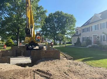 On a residential street, an excavator works on digging out a trench.