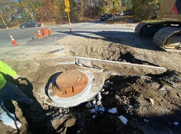 A rough hole in a street, with a concrete circle and a metal cap on that.