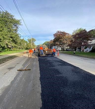 As the asphalt is laid, workers rack and smooth out a strip down the middle of the street.