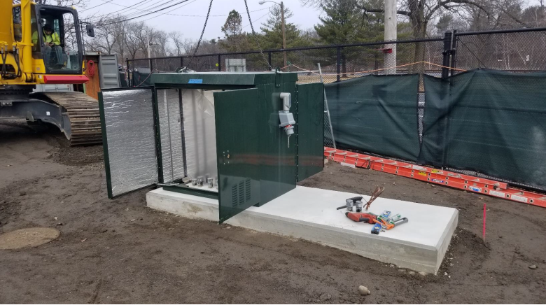 On a concrete slab there is a green, metal, insulated cabinet.