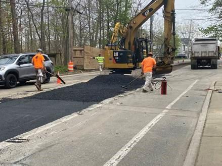 Workers smooth out a strip of fresh asphalt down the centre of a street.