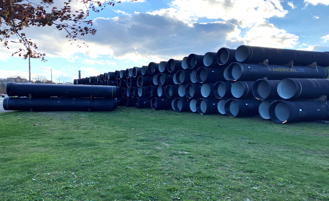 A large stack of black pipes on a grass yard.