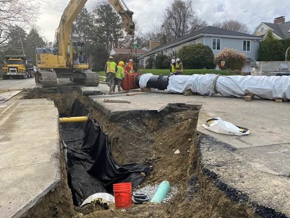 A black pipe wrapped in white plastic gets inspected before being put in an excavated hole. 