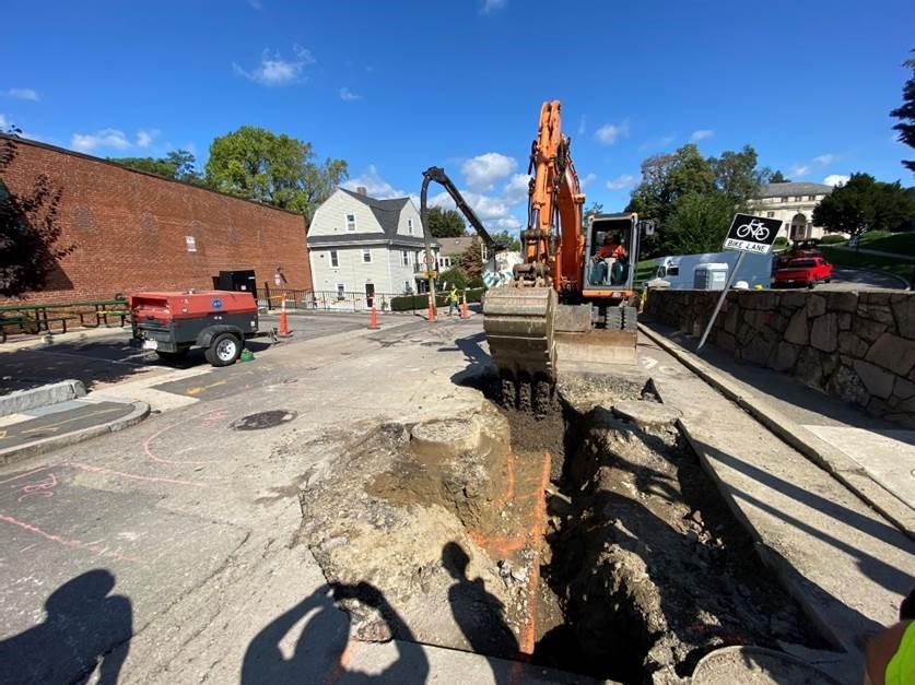 A digger breaks through sidewalk to begin excavating a pit. 