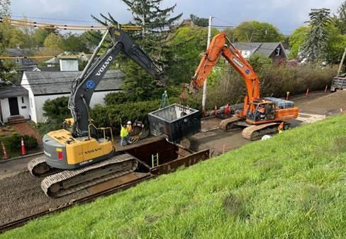 Two excavators work over a pit on a residential street. 